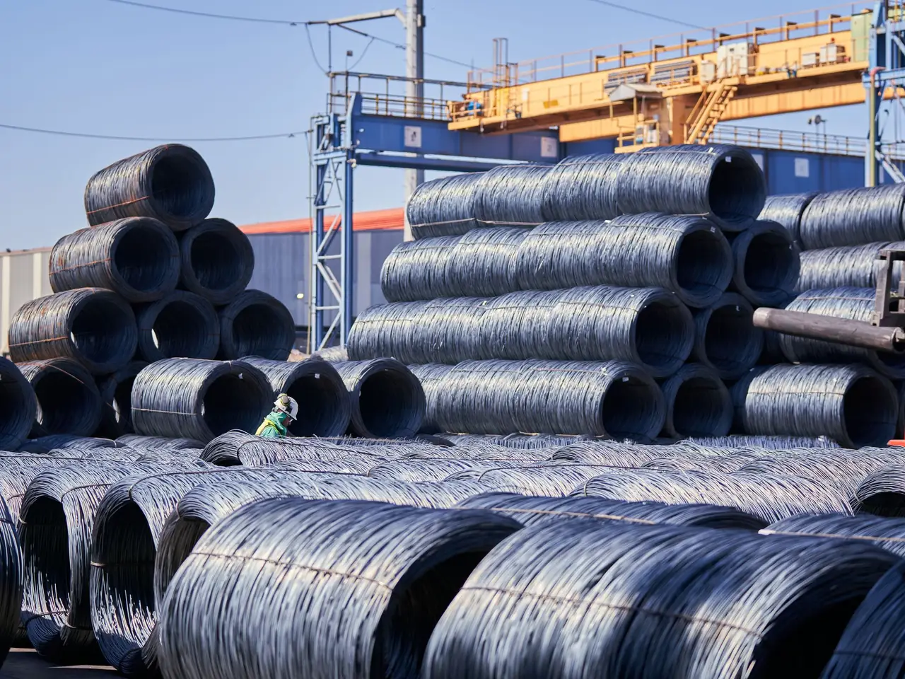 Wire rod coils stacked in a mill yard under a gantry crane